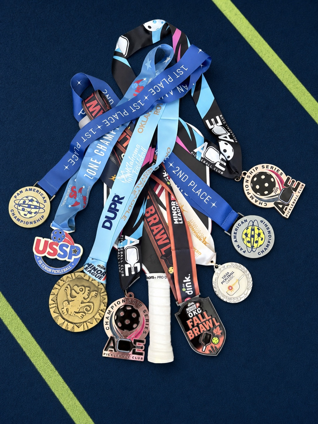 Pickleball paddle covered in tournament medals on a navy court